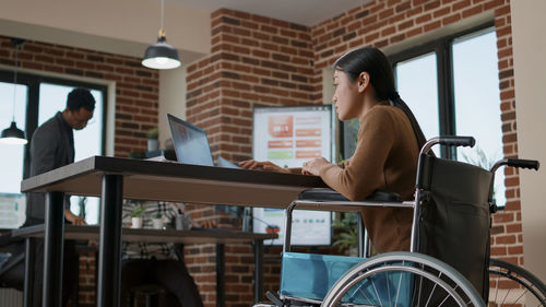 Side view of woman using laptop while sitting on wheelchair