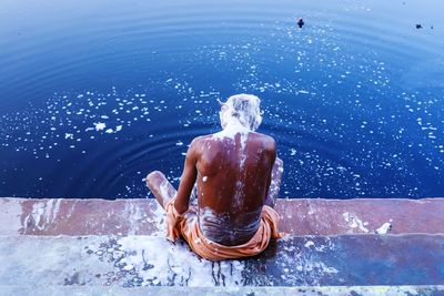 Rear view of shirtless soapy man bathing on riverbank