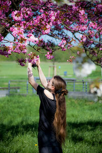 Full length of woman standing by pink flowers on field