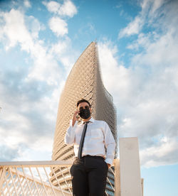 Low angle view of man standing by railing against sky