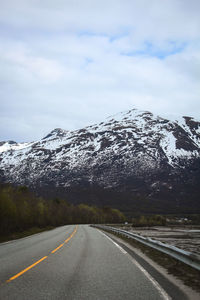 Road by snowcapped mountains against sky