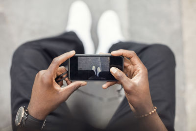 High angle view of man photographing legs on mobile phone