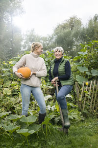 Happy young woman with her grandmother holding pumpkin in garden