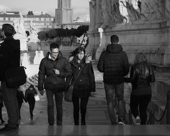 Rear view of people walking by buildings in city