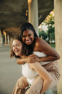Portrait of happy teenage girl giving piggyback ride to female friend