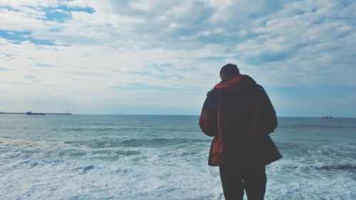 Rear view of man standing on beach against sky