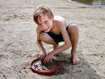 Full length portrait of boy cleaning worms in tray at sandy beach