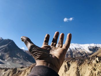 Cropped hand of man gesturing towards mountains and blue sky