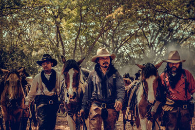 Cowboys standing with horse in forest