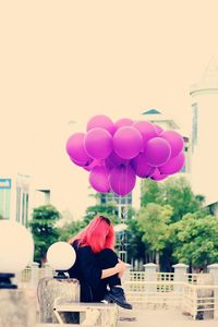 Rear view of woman with balloons standing against sky in city