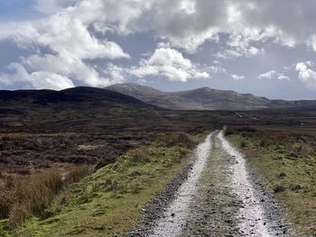 Road passing through landscape against cloudy sky