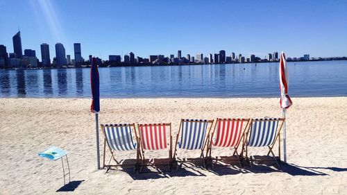 View of beach chairs on sand in city against skyline