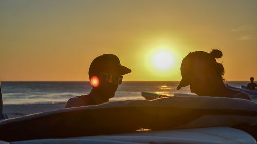 Friends sitting at beach against sky