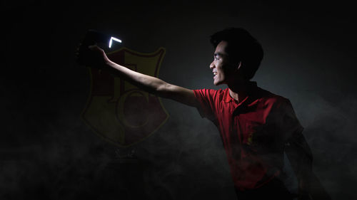 Side view of young man standing against black background