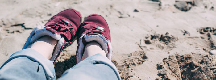 Low section of woman wearing shoes on sand