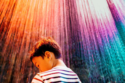 Low angle view of boy looking down while standing against illuminated wall