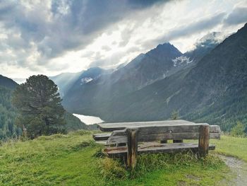 Empty bench on field by mountains against sky