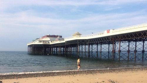 Woman standing on beach by bridge against sky