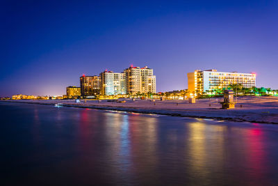 Illuminated buildings by sea against clear sky at night