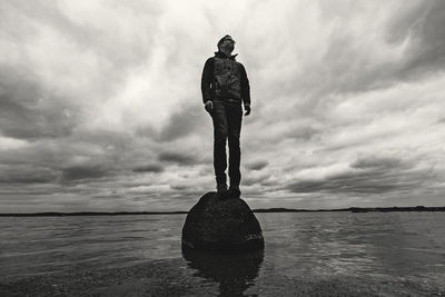 Man stands on rock in middle of lake with storm clouds looming