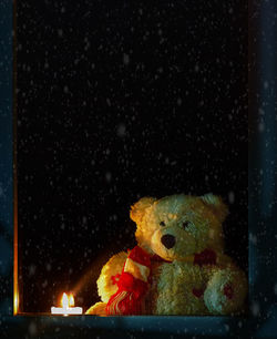 Teddy bear by lit candle seen through window glass during winter