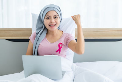 Portrait of smiling young woman using laptop on bed
