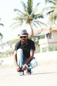 Portrait of man in sunglasses tying shoelace at beach against sky