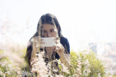 Portrait of young woman photographing through mobile phone