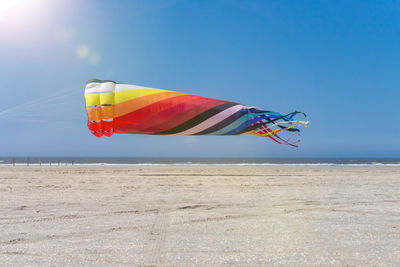 Low angle view of multi colored kite at beach against blue sky