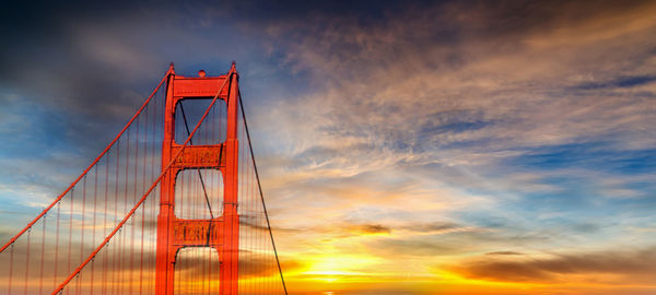 Low angle view of suspension bridge against cloudy sky