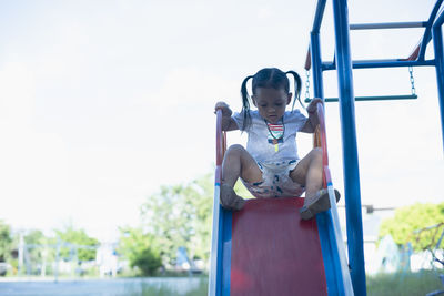 Portrait of young woman sitting on railing against sky