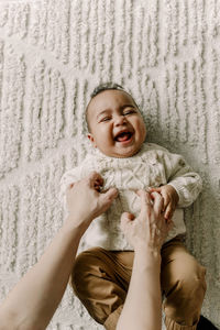 Cropped image of mother tickling baby boy lying on blanket