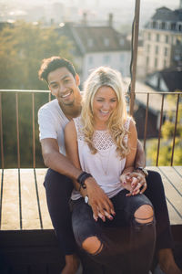 Portrait of smiling young couple sitting in city