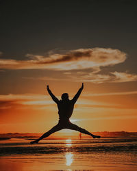 Silhouette woman with arms outstretched standing on beach against sky during sunset