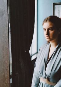 Reflection of beautiful young woman standing against window at home in mirror