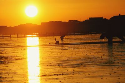 Silhouette people on beach against orange sky