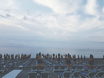 Lounge chairs and parasols arranged on sand against sea during sunset