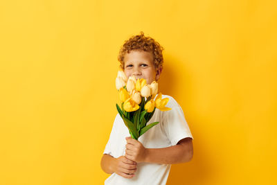 Portrait of young woman holding yellow flower against orange background