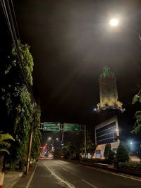 Illuminated road by buildings against sky at night