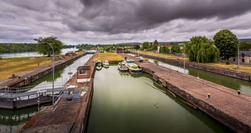 High angle view of river amidst trees with long boat parked against sky