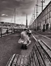 Rear view of woman sitting on sidewalk in city against sky