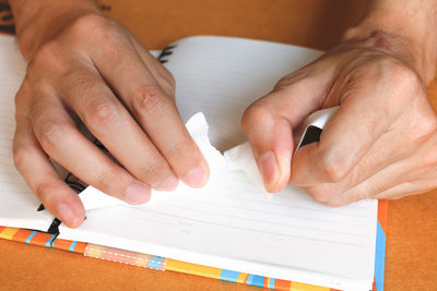 Close-up of cropped hands tearing page of book on desk