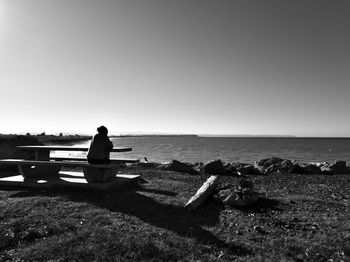 Rear view of man sitting on beach against clear sky