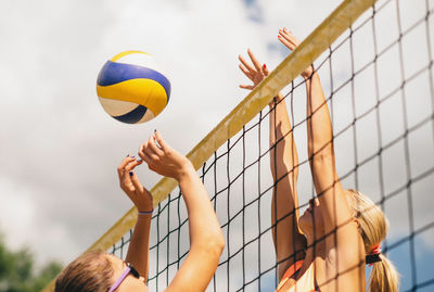 Low angle view of women playing beach volleyball against sky