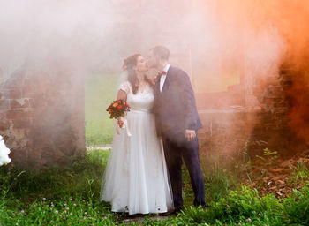 Full length of newlywed couple standing by abandoned built structure