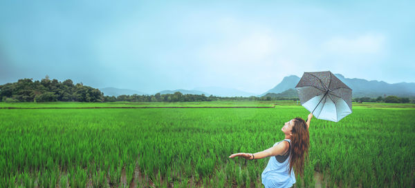 Rear view of woman with arms outstretched standing on field against sky