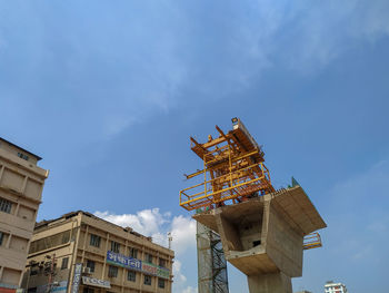 Low angle view of crane by building against sky