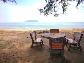 Chairs and table at beach against sky