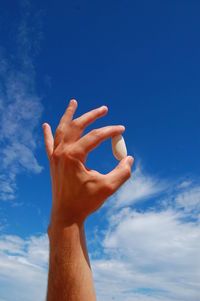 Low angle view of hand holding stone against blue sky