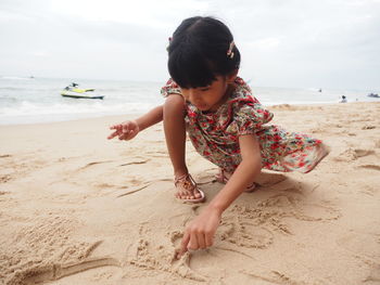 Full length of girl playing with sand on beach against sky